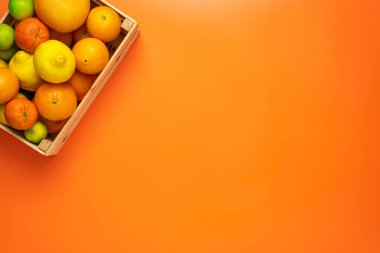 Taze, meyveli ve sulu meyve kavramı. Üst Manzara. Resmin sol üst köşesinde turuncu arka planda taze turunçgil meyveleriyle dolu küçük tahta bir kutu.