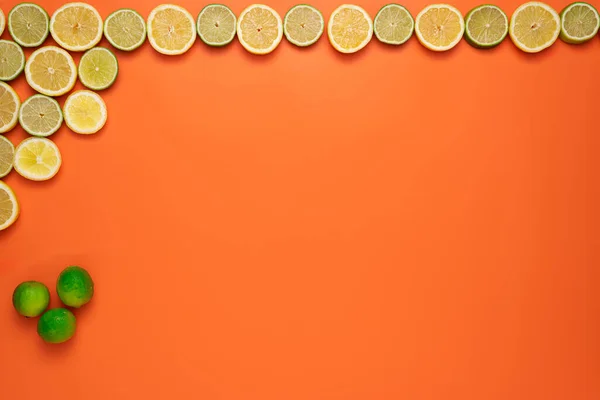 Fresh, Fruity and juicy fruit concept. View from top. Freshly cut slices of lemons and limes on the upper and left border of the image on an orange background.