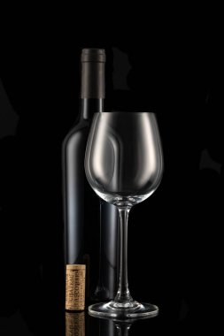 Kapalı bir şarap şişesi, şarap kadehi ve siyah arka planda şarap mantarı.