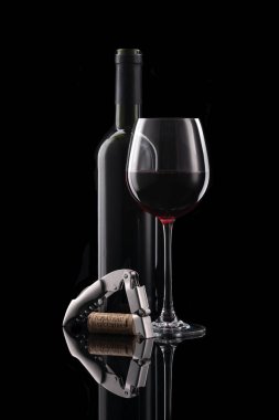 Açık bir şişe kırmızı şarap ve siyah arka planda metal bir tirbuşon seti olan bir kadeh şarap.