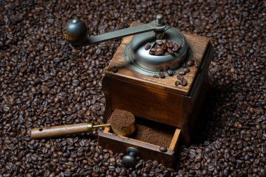 Bir sürü kahve çekirdeğinin arka planında elinde kaşık olan eski bir kahve öğütücüsü duruyor.