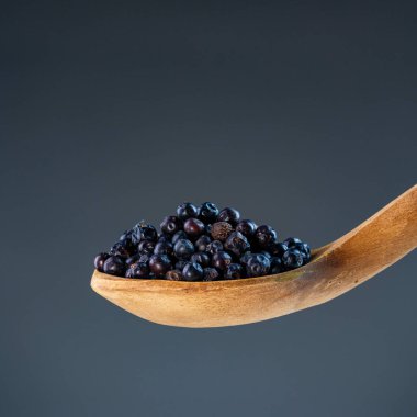 Doğal ahşap kepçe içinde taze kurutulmuş ardıç meyveleri. Mutfak otları ve aromatik yemek malzemeleri için ideal.