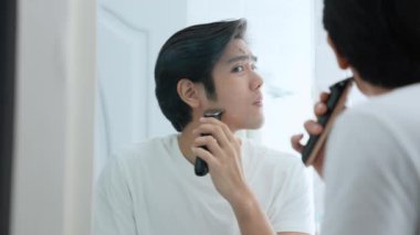Sağlık konsepti 4k Çözünürlük. Genç Asyalı adam banyoda tıraş oluyor. Aynaya bak. elektrikli traş makinesi.