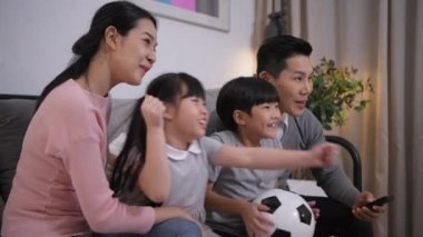 Aile kavramı 4k Kararlılığı. Asyalı ebeveynler ve çocuklar tatilde evde futbol maçı izliyorlar..