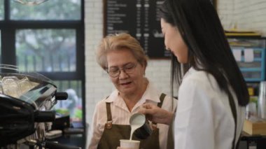 Coffee shop concept of 4k Resolution. An old woman teaching a young female employee to make coffee in a shop.