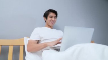 Tatil konsepti 4k Çözünürlük. Asyalı adam yatak odasında video görüşmesi için bilgisayar kullanıyor..