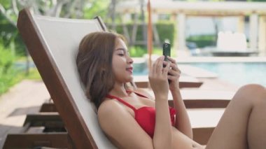 Holiday concept of 4k Resolution. Asian woman in bikini playing mobile phone by the pool.