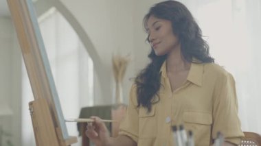 Sanatçı konsepti 4k Çözünürlük. Asyalı kadın oturma odasında resim çiziyor. Sanatçı iş yaratıyor. Boş zaman aktiviteleri ve hobileri.