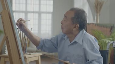 Sanatçı konsepti 4k Çözünürlük. Asyalı adam oturma odasında resim yapıyor. Sanatçı iş yaratıyor. Boş zaman aktiviteleri ve hobileri.