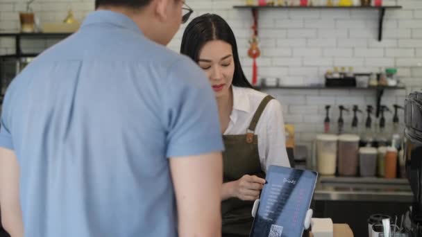 4K解像度のコーヒーショップのコンセプト アジアの女性従業員が店舗でタブレットを使用して顧客にメニューを紹介しています — ストック動画