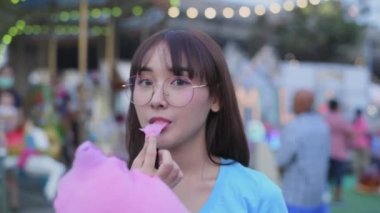 Tourism concept of 4k Resolution. Asian woman eating cotton candy happily in amusement park.