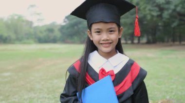 Eğitici 4k çözünürlük kavramı. Mezuniyet elbisesi giymiş Asyalı bir kız bahçede kendine güvenle gülümsüyor..