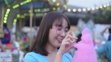 Tourism concept of 4k Resolution. Asian woman eating cotton candy happily in amusement park.