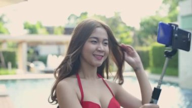 Tatil konsepti 4k Çözünürlük. Bikinili Asyalı kadın havuz başında cep telefonuyla canlı bir görüşme yapıyor..