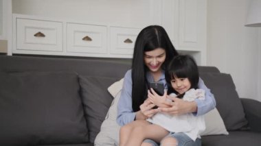 Family concept of 4k Resolution. Asian mother and daughter playing mobile phones in the living room.