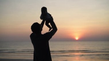 4k Kararlılığın Turizm kavramları. Asyalı bir babanın silueti bebeğini kumsalda tutuyor..