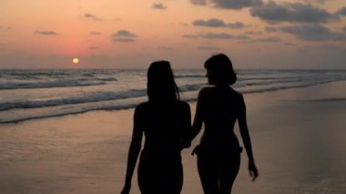 Tatil konsepti 4k Çözünürlük. Sahilde yürüyen iki kızın silueti..