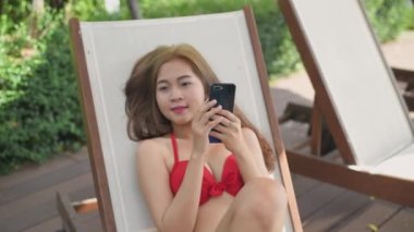 Holiday concept of 4k Resolution. Asian woman in bikini playing mobile phone by the pool.