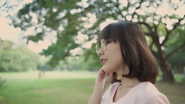 4K解像度の休日の概念 庭にはヘッドフォンをしているアジアの女性 彼女はオンラインで音楽を聴いています — ストック動画