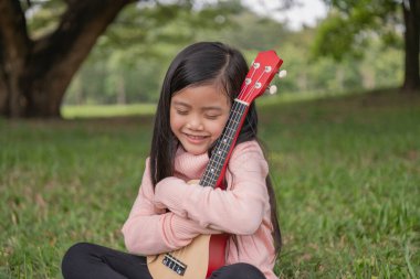 Bahçede ukulelesini kucaklayan Asyalı kız. Müzik çalmayı seviyor..