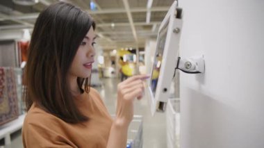 Alışveriş konsepti 4k Çözünürlük. Asyalı kadın alışveriş merkezindeki tabletle fiyatları kontrol ediyor.