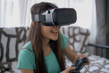 Asyalı kadın oturma odasında VR ile oyun oynuyor..