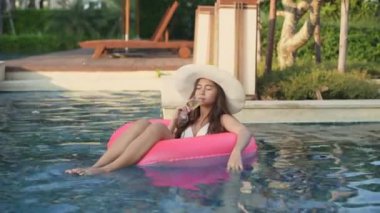 Holiday concept of 4k Resolution. Asian woman in bikini drinking cocktail while swimming in the pool.