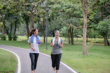 İki kadın yemyeşil bir parkta koşuyor.