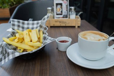Bir fincan kahveyle servis edilen bir tabak altın patates, sıcacık bir kafede mükemmel bir aperatif anı yakalıyor..