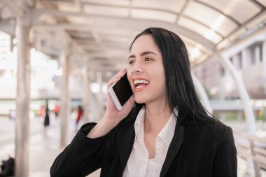 Profesyonel bir kadın, modern bir şehir ortamında akıllı telefonuyla iletişim kurarak kendine güvenini gösteriyor..