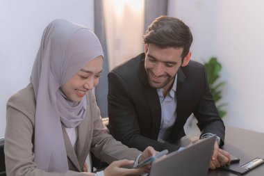 Bir ofis ortamında işbirliği yapan, fikir alışverişinde bulunan ve dijital bir cihaz üzerinde birlikte çalışan iki profesyonel..