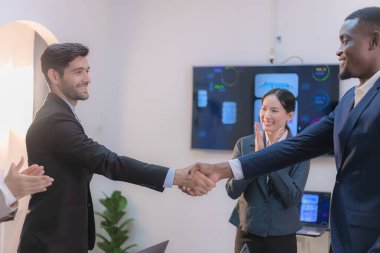 Modern bir ofiste, başarılı bir iş anlaşmasını ve işbirliğini simgeleyen iki profesyonel el sıkışıyor..