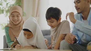 İslami öğrenme konsepti 4k çözünürlük. Asyalı Müslüman bir aile deftere birlikte kelimeler yazarak eğleniyor..