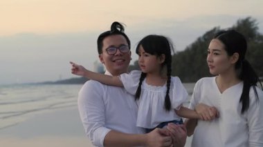 Tatil konsepti 4k Çözünürlük. Anne ve babalar sahilde yürüyüş için kızlarını kucağına alıyorlar. Yaz tatili.