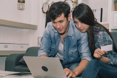 Genç bir çift birlikte online alışveriş yapmayı, bir dizüstü bilgisayarı paylaşmayı ve rahat bir oturma odasında seçenekleri tartışmayı seviyor..