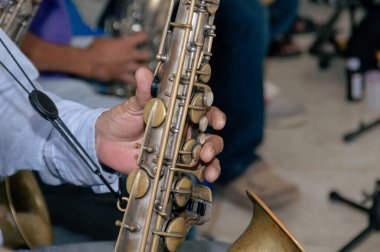 Saksafon çalan bir müzisyenin elinin yakın çekimi enstrümanın karmaşık anahtar ve detaylarını gözler önüne seriyor..