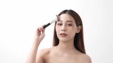 4k Çözünürlük 'ün güzellik konsepti. Beyaz bir arka planda fırçayla makyaja gülen Asyalı kadın..