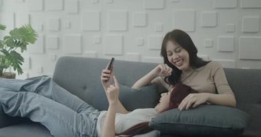 4k Çözünürlük ev arkadaşı konsepti. Asyalı kızlar oturma odasında cep telefonlarıyla oynuyorlar..