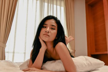 Yatakta rahat bir kadın, pencereden süzülen doğal ışığın tadını çıkarıyor, huzur ve huzuru somutlaştırıyor..