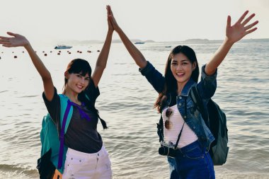 İki kadın sevinçle plaj günlerini kutluyorlar. Işıl ışıl kıyı şeridinde mutluluk ve dostluğu ifade ediyorlar..