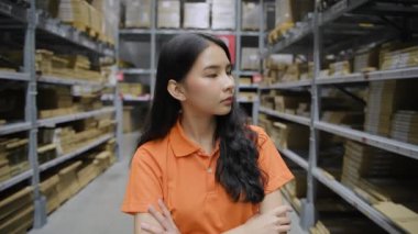 Alışveriş konsepti 4k Çözünürlük. Asyalı kadın çalışan depoda dolaşıyor, ürünleri kontrol ediyor ve düşünüyor..