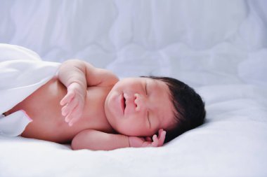 Huzurlu, yeni doğmuş bir bebek. Yumuşak, beyaz bir battaniyenin üzerinde rahat bir şekilde uyuyor. Masumiyet ve sükuneti somutlaştırıyor..