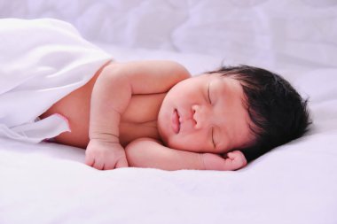 Huzurlu, yeni doğmuş bir bebek yumuşak beyaz bir battaniyenin üzerinde mışıl mışıl uyuyor. Eski hayatın masumiyetini somutlaştırıyor..