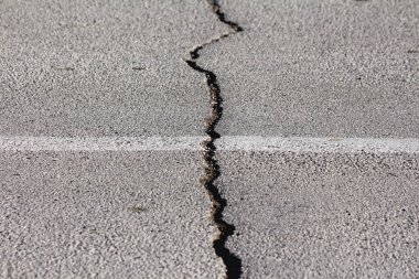 Büyük bir deprem sonrası ortaya çıkan asfalt yolda sıcak kış gününde doldurulmayı ve onarılmayı bekleyen büyük bir çatlak.