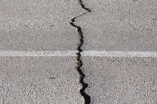 stock image Large crack on public paved asphalt road that appeared after big earthquake waiting to be filled and repaired on warm sunny winter day