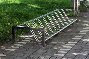 Yeni modern zemin monte edilmiş bisiklet standı ya da taştan fayansların üzerindeki kaldırımda güneşli bir bahar gününde yerel halk parkındaki işlenmemiş çimlerin yanında bisiklet askısı.
