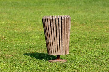 Yerel halk parkında beton temele monte edilmiş dar dikey ahşap tahtalardan yapılmış eski, harap çöp tenekesi sıcak yaz gününde taze kesilmiş çimlerle çevrili.