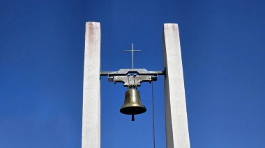 Pirinç çan ve metal haçlı minimalist beyaz çan kulesi, çağdaş kilise mimarisinde inanç ve basitliği simgeleyen derin mavi gökyüzüne karşı dimdik ayakta duruyor..
