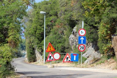 Kayalık ormanın içinden geçen dar asfalt yol kıvrımları, 5t ağırlık limiti ve inşaat alanına giriş saatinde 20 km / saat kısıtlama da dahil olmak üzere sayısız yol çalışması, uyarı ve hız limiti işareti içeriyor.