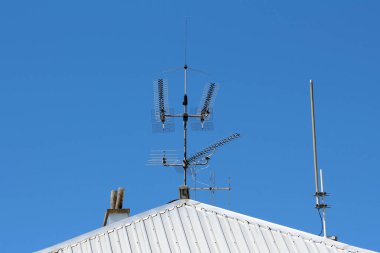 Beyaz metal çatıya monte edilmiş modern televizyon ve radyo anten kümeleri bulutsuz mavi gökyüzüne keskin bir şekilde karşı, iletişim teknolojisini temsil ediyor.